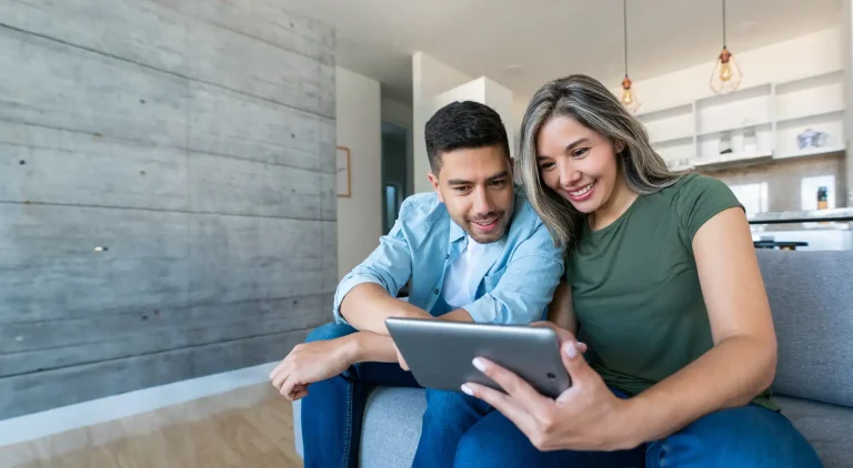 Happy Latin American couple at home watching videos on a tablet and smiling