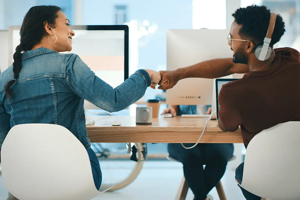 two young designers giving each other a fist bump in an office