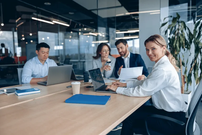 Mujer de negocios sonriente y segura de sí misma sentada en la oficina con un grupo de colegas.